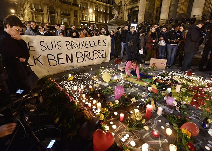 People holding a banner reading I am Brussels behind flowers and candles to mourn for the victims at Place de la Bourse in the center of Brussels, Tuesday, March 22, 2016. Bombs exploded at the Brussels airport and one of the citys metro stations Tuesday, killing and wounding scores of people, as a European capital was again locked down amid heightened security threats. (AP Photo/Martin Meissner)