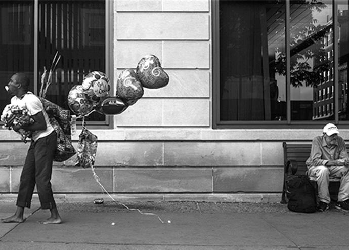 Performers playing trumpets and carrying balloons walk past a man sitting on a Dubuque Street bench on June 18. (The Daily Iowan/Jordan Gale)  