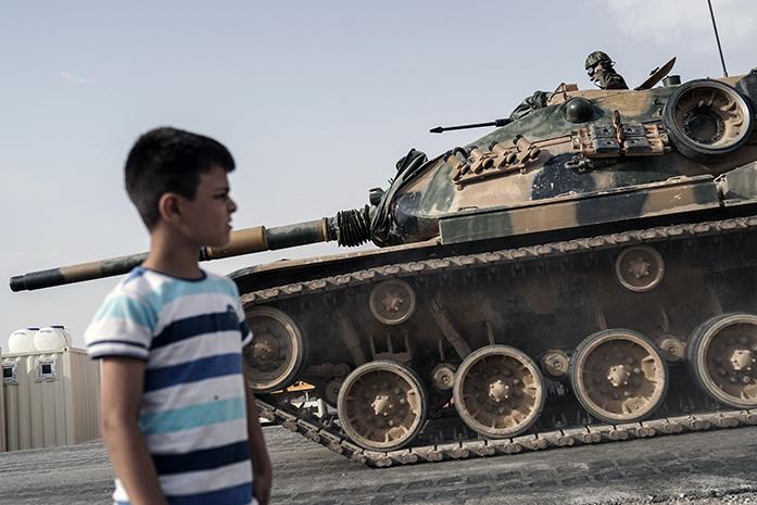 A boy looks at Turkish army tanks and armored personnel carriers moving toward the Syrian border, in Karkamis, Turkey, Thursday, Aug. 25, 2016. Turkish President Recep Tayyip Erdogan late Wednesday said that Syrian opposition forces aided by Ankara have taken back the border town of Jarablus from the Islamic State group. Erdogan said the Syrian rebels, together with those who are from Jarablus, have now taken it back and IS has been forced to leave Jarablus. (AP Photo/Halit Onur Sandal)