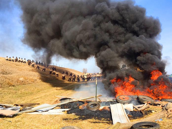 Tires+burn+as+armed+soldiers+and+law+enforcement+officers+stand+in+formation+on+Thursday%2C+Oct.+27%2C+2016%2C+to+force+Dakota+Access+pipeline+protesters+off+private+land+where+they+had+camped+to+block+construction.+The+pipeline+is+to+carry+oil+from+western+North+Dakota+through+South+Dakota+and+Iowa+to+an+existing+pipeline+in+Patoka%2C+Ill.+%28Mike+McCleary%2FThe+Bismarck+Tribune+via+AP%29