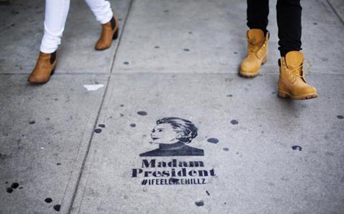 Pedestrians walk past a sidewalk message depicting Democratic presidential candidate Hillary Clinton a few blocks from her planned election night rally in New York, Tuesday, Nov. 8, 2016. (AP Photo/David Goldman)