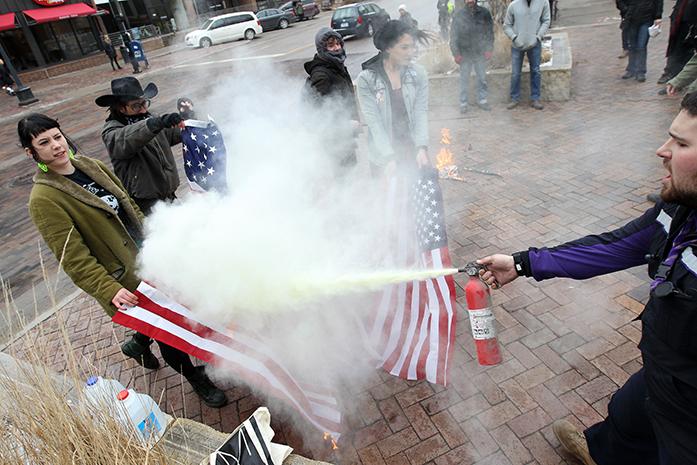 Matt Uhrin extinguishes a set of American flags being set on fire by protesters on the pedestrian mall along Clinton Street on Thursday, Jan. 26, 2017. (David Scrivner/Iowa City Press-Citizen)
