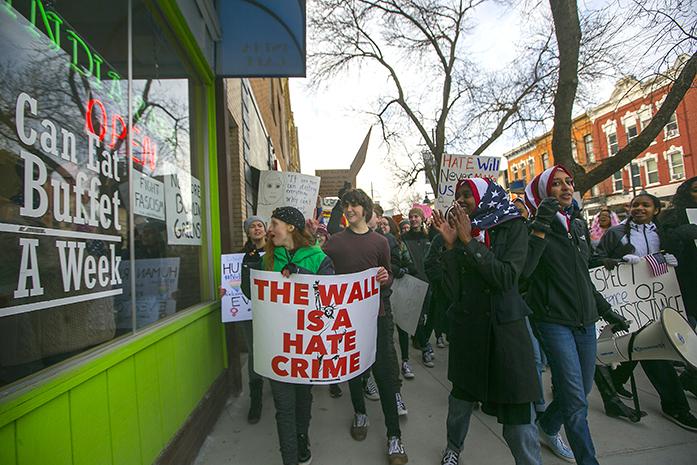 West High sophomore Ala Mohamed cheers on a woman inside restaurant holding a Fight Fascism sign during the Solidarity Against the Ban march downtown on Sunday, Feb. 5, 2017. More than one thousand people attended the march. (The Daily Iowan/Joseph Cress)