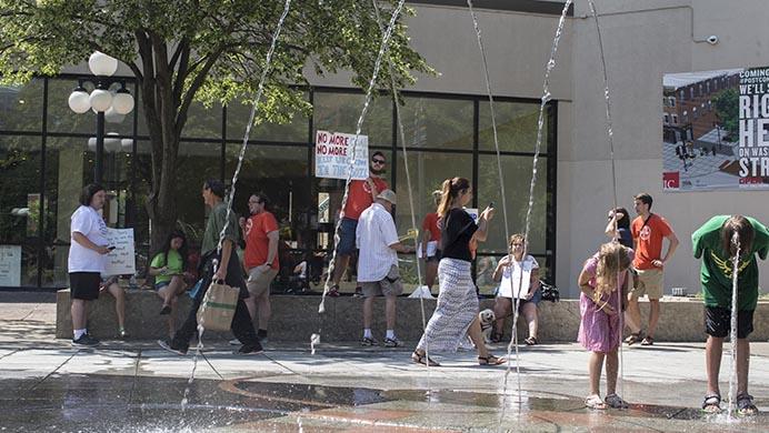 Children play in the water fountain while Judd Hayes from NextGen Climate holds a sign on the Pedestrian Mall prior to their anti Donald Trump protest on Thursday, July 21, 2016.  NextGen organized four protests in Iowa against the Republican nominee in Des Moines, Ames, Iowa City and Waterloo. (The Daily Iowan/Joseph Cress)