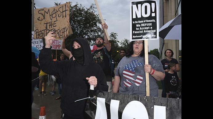 A masked protestor holds a sign outside of Protestors hold signs outside of a Donald Trump rally in Cedar Rapids on Wednesday June 21, 2017. (Nick Rohlman/The Daily Iowan)