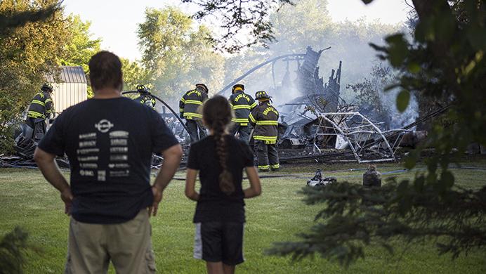 Mike Tingley, the homeowner, stands with his daughter as they watch the Grand Blanc Fire Department put out his garage fire with assistance from Burton and Mundy Township on the 6000 block of Grove Avenue in Grand Blanc Township, Mich., on Monday evening, July 3, 2017. Grand Blanc Fire Chief Bob Burdette says the homeowner was trying to use a smoke bomb to get a bees nest out of the garage.  (Shannon Millard/The Flint Journal-MLive.com via AP)