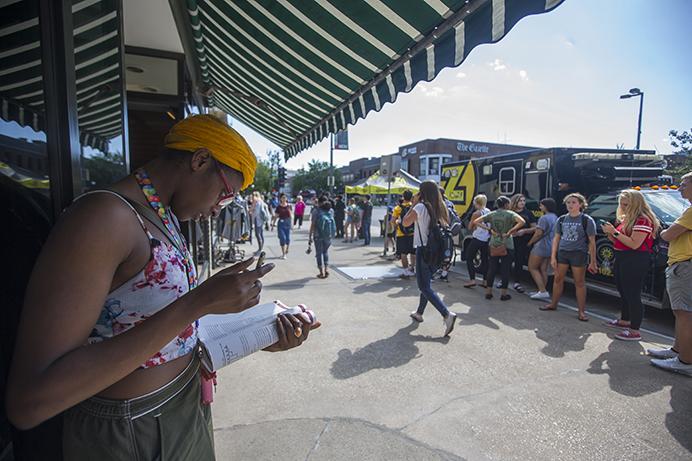 UI grad Tayo Ajose studies in the shade while waiting in line for burritos while her boyfriend holds her spot in line outside Pancheros Mexican Grill on Clinton Street on Tuesday, Aug. 22, 2017. Pancheros has been celebrating their 25th anniversary all month with promotions like free queso on their anniversary, and $1 burritos at their downtown Iowa City location yesterday. (Joseph Cress/The Daily Iowan)