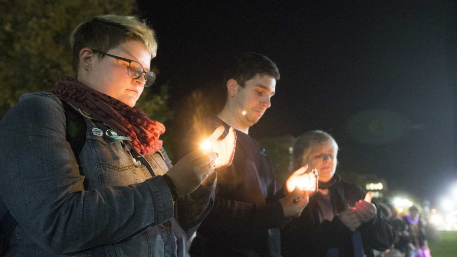 From left: UI senior Ellen Kuehnle and Women's Resource and Action Center employees Cody Howell and Laurie Haag hold candles during the UI Sister Vigil for Survivors of Campus Sexual Assault on the Pentacrest on Tuesday, Oct. 17, 2017. The event included letter writing to Iowa senators and the signing of thank you state of Iowa flags to senators fighting the withdrawal of Title IX protections for survivors of sexual assault. (Lily Smith/The Daily Iowan)