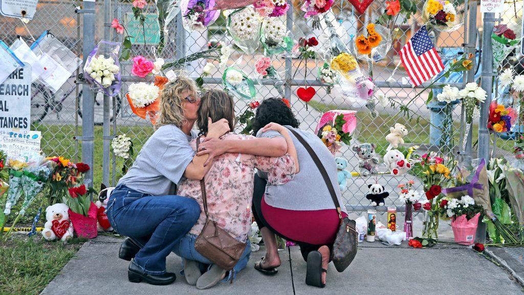Shari Unger kisses Melissa Goldsmith as Giulianna Cerbono lights candles at a memorial at Marjory Stoneman Douglas High School on Sunday, February 18, 2018. A large number of people visited the site to honor the students and teachers killed in a shooting spree on Wednesday, February 14, 2018. (Charles Trainor Jr./Miami Herald/TNS)