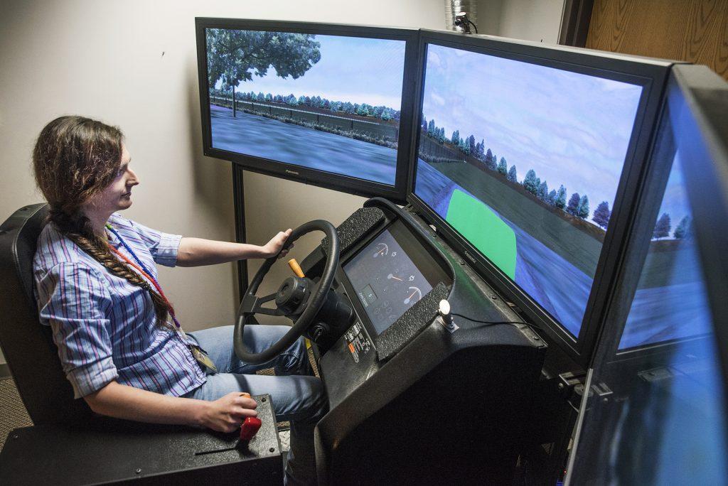 Kayla Faust operates the miniSim, one of only two such driving simulators in the world, at the National Advanced Driving Simulator in Coralville, Iowa. Designed to puts farmers on virtual roads and fields, the miniSim uses steering, pedals, shifters, and a seat from an actual tractor to replicate potentially dangerous driving situations. Faust hopes to find changes that need to be made in farming equipment to avoid accidents. (The Daily Iowan/Olivia Sun)