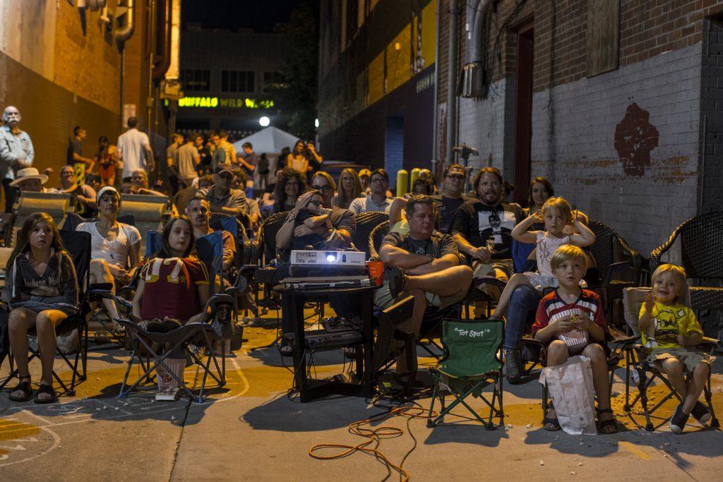 Partygoers watch a movie projected in the ally behind The Film Scene during the Iowa City Downtown District Block Party on Saturday June 23, 2018. The 2nd annual event during which open containers were allowed in a select portion of downtown attracted thousands of guests and featured a variety of activities and performances. (Nick Rohlman/The Daily Iowan)