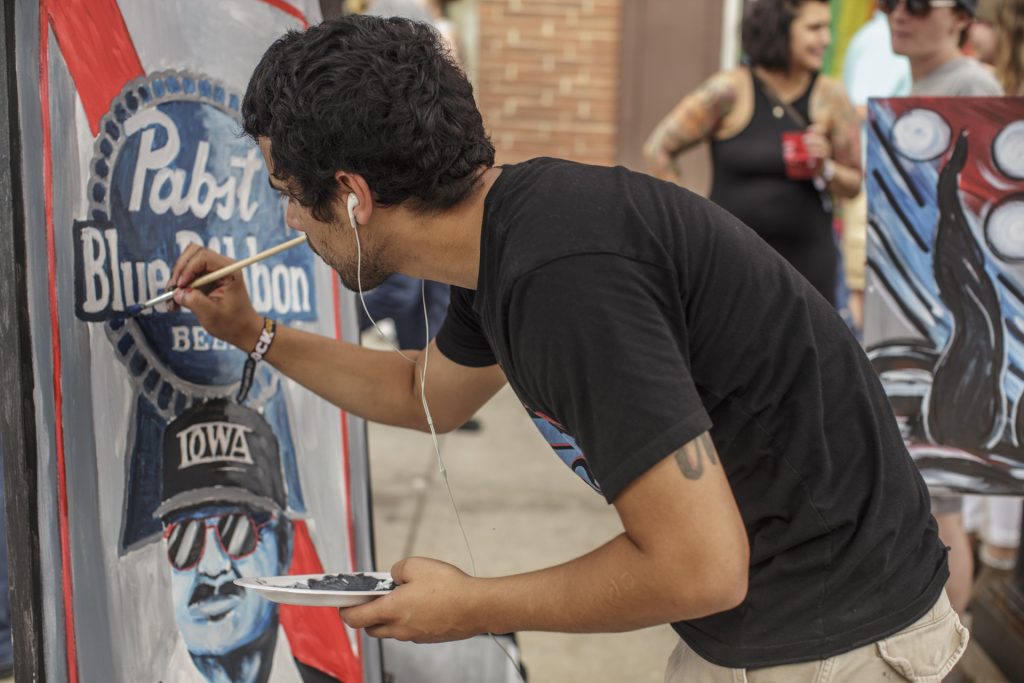 An artist paints a portrait of Hayden Fry during a "Live Painting" demonstration during the Iowa City Downtown District Block Party on Saturday June 23, 2018. The 2nd annual event during which open containers were allowed in a select portion of downtown attracted thousands of guests and featured a variety of activities and performances. (Nick Rohlman/The Daily Iowan)