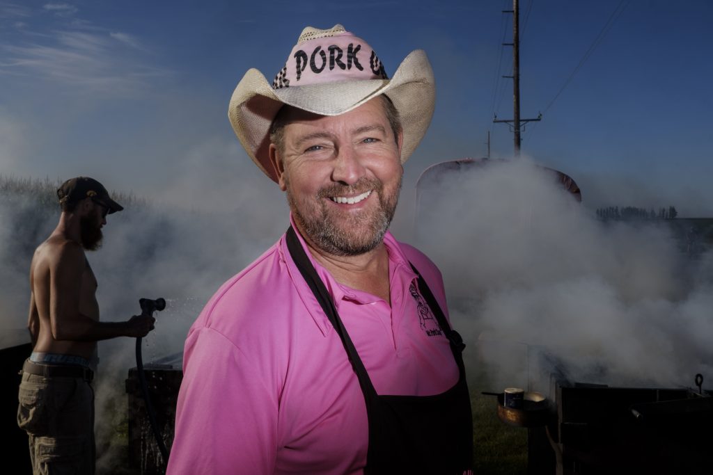 Matt Bernhard a.k.a. Mr. Pork Chop poses for a portrait outside of Wellman, Iowa along the RAGBRAI route on Friday, July 27, 2018. Bernhard inherited the Mr. Pork Chop title from his father Paul who began selling pork chops on the RAGBRAI route in 1983. ÒWhen they come over the hill they see the smoke and they see the pink bus and they know itÕs meÓ Bernhard said. ÒWeÕve been here 35 years, weÕre part of RAGBRAI.Ó (Nick Rohlman/The Daily Iowan)