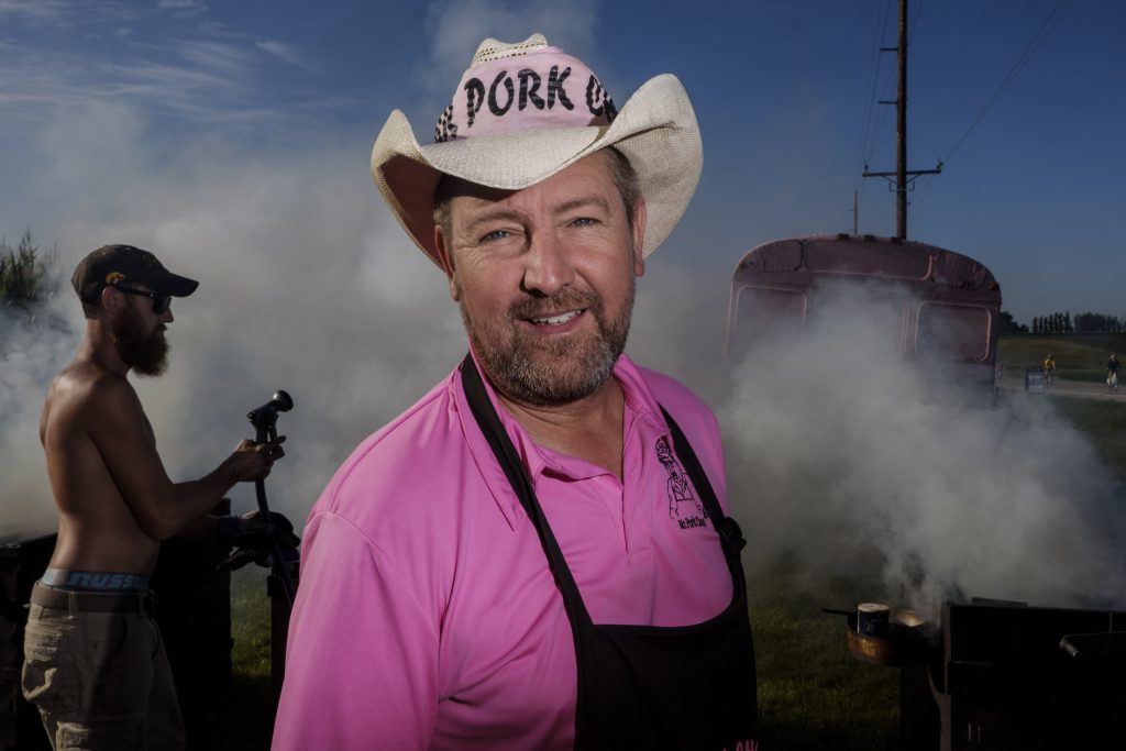 Matt Bernhard a.k.a. Mr. Pork Chop poses for a portrait outside of Wellman, Iowa along the RAGBRAI route on Friday, July 27, 2018. Bernhard inherited the Mr. Pork Chop title from his father Paul who began selling pork chops on the RAGBRAI route in 1983. ÒWhen they come over the hill they see the smoke and they see the pink bus and they know itÕs meÓ Bernhard said. ÒWeÕve been here 35 years, weÕre part of RAGBRAI.Ó (Nick Rohlman/The Daily Iowan)