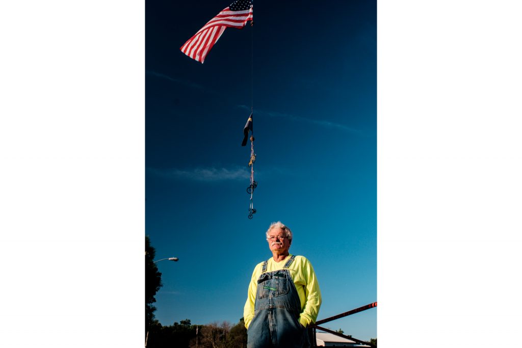 Jim Townsend poses in front of his crane holding a chain of bicycles and an American flag, in Wellman, Iowa on the morning of Friday, July 27, 2018 as riders began trickling in to town. Jim provided this display and other supplies for free, explaining, Its RAGBRAI. When its your hometown, you got to do your part. Jim is the owner of Townsend Cranes. Riders rode from Sigourney to Iowa City on Day 6 of this years ride. (Jared Krauss/The Daily Iowan)