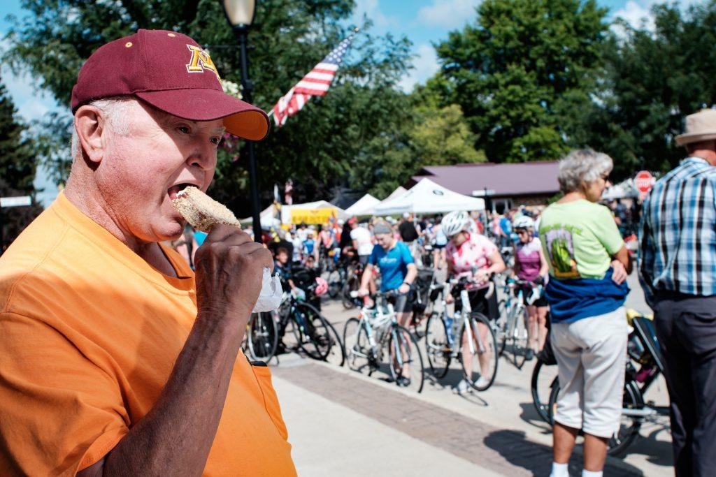 Charles Rhodes of Yuma, Arizona is seen eating a Kalona bar in Kalona, Iowa, while watching riders from RAGBRAI fill the town on Friday, July 27th, 2018. Charles, who was just in town to visit friends, was surprised to learn there would be 20,000 riders passing through. Riders rode from Sigourney to Iowa City on Day 6 of this years ride. (Jared Krauss/The Daily Iowan)