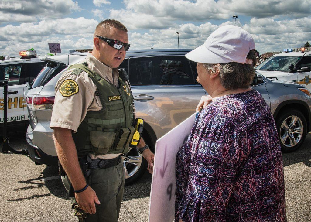 An attendee holds a sign in front of an officer outside of Northeast Iowa Community College in Peosta on July 26, 2018. Both pro- and anti-Trump demonstrators were present for the arrival of the president. (Katina Zentz/The Daily Iowan)