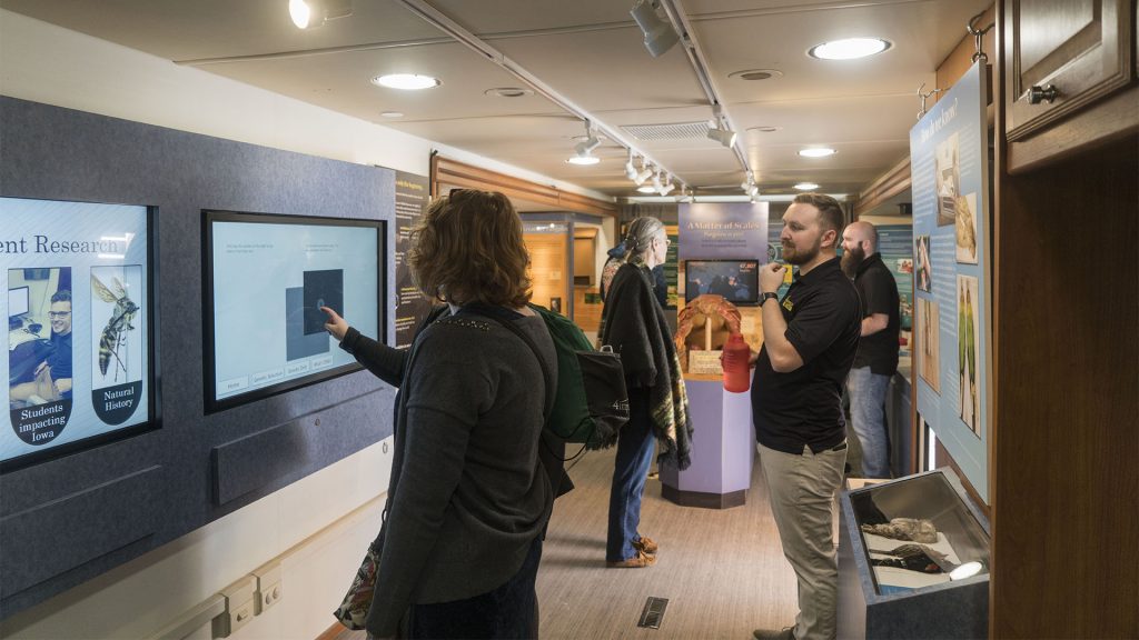 A staff member watches a visitor operate the touch screen in the UI Mobile Museum on Wednesday, April 11, 2018. (The Daily Iowan/Gaoyuan Pan)