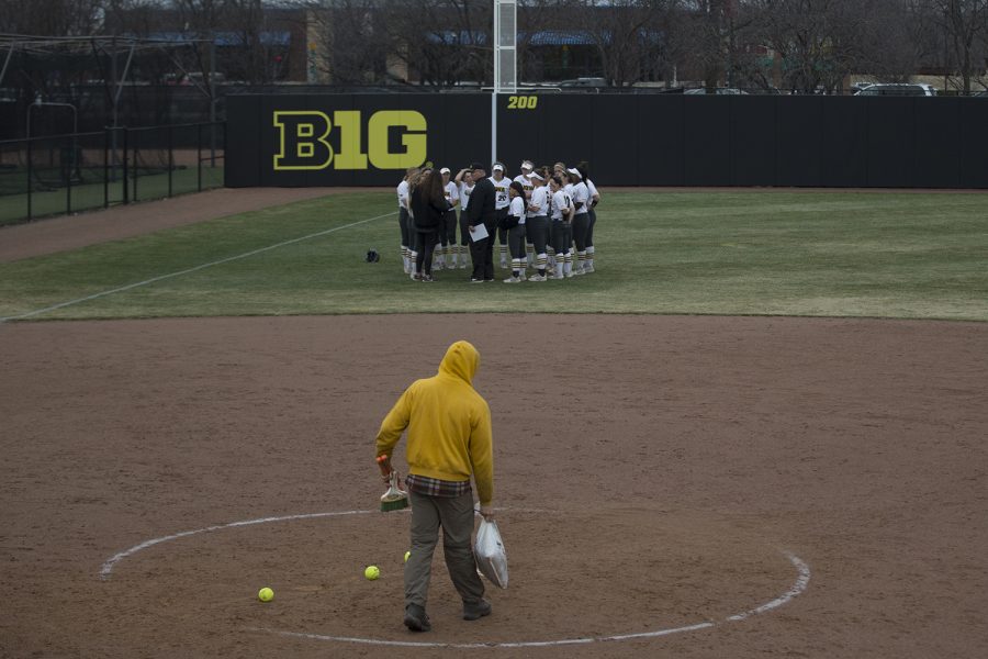 Workers clean the field as the Hawkeyes huddle after the conference opening softball game at Pearl Field on Friday, March 29, 2019. The Wildcats defeated the Hawkeyes 5-1.