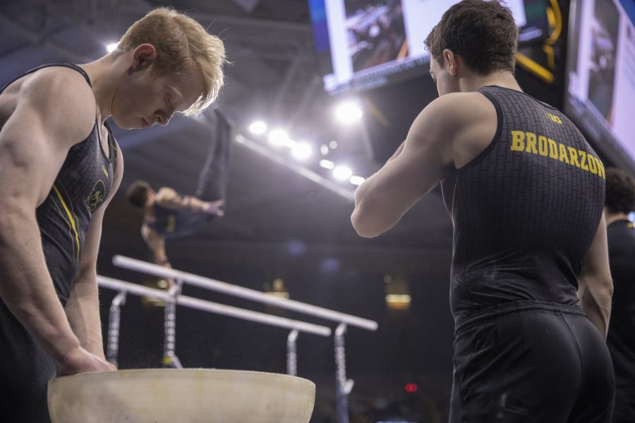 Hawkeye gymnasts Nick Merryman and Jake Brodarzon chalk up their hands while teammate Stewart Brown warms up Friday in Carver Hawkeye Arena during the Men's Big Ten Championships. Penn State won the team competition with a combined score of 410.350 points. 