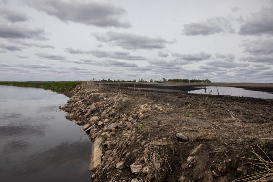 A cornfield on the right side of the picture is affected by standing water from recent rainfall. To the left side of the picture, the rocky bank of the cornfield meets the Iowa River.