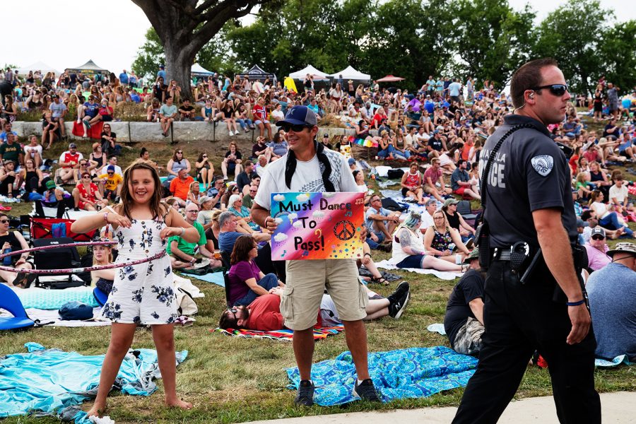 An attendee at Hinterland holds up a sign that reads,Must Dance To Pass on August 3, 2019 in Saint Charles, Iowa. A cop walks past and disobeys the signs request.