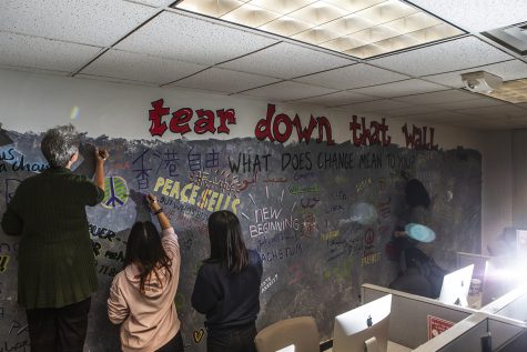 Attendees write on the Berlin Wall artwork in Phillips Hall on Thursday. Members of the community contributed to the piece by adding words regarding their feelings about the relationship between the tearing down of the Berlin Wall and President Trump’s efforts to build a wall. 