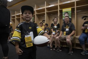 Kid Captain Jeg Weets poses for a picture while his mother and father sit behind him in the Hawkeye football locker room at Kids Day at Kinnick on Saturday, August 10, 2019. Kids Day at Kinnick is an annual event for families to experience Iowas football stadium, while watching preseason practice and honoring this years Kid Captains.
