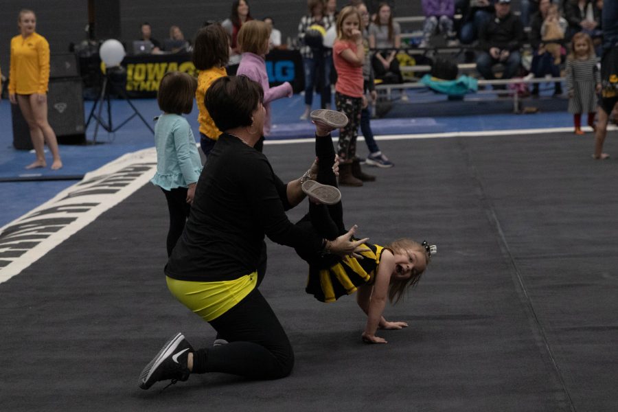 Iowa gymnastics assistant coach Jennifer Green supports a young Gymhawks fan while she competes in a handstand contest during an inter-squad gymnastics meet on Saturday, Dec. 7, 2019 at the Field House. The gold team defeated the black team 7-6. 