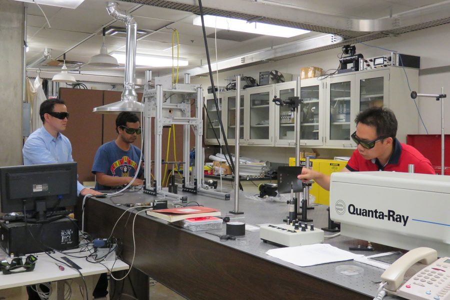 Professor Hongtao Ding (left), PhD students Avik Samanta (center) and Qinghua Wang (right) work on a nanosecond laser surface treatment system to conduct experiments in Ding’s laser research lab in the IATL building. (Contributed)