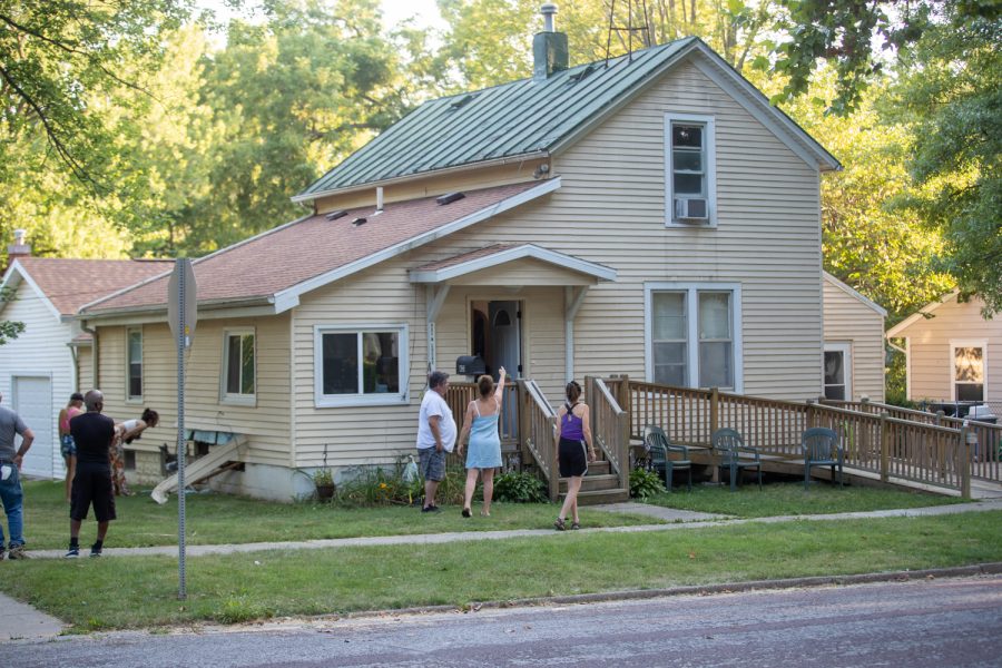 Neighbors stand on a property after an FBI raid in Iowa City on Wednesday, Aug. 18. Damage can be seen on the side of the house after being hit by an armored truck during the raid.