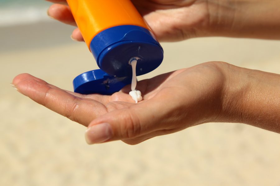 Woman holding and applying suntan lotion on a beach.