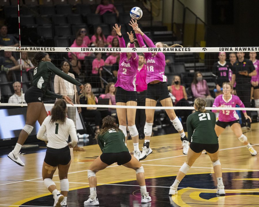 Michigan State outside hitter Biamba Kabengele hits the ball towards Iowa middle back Hannah Clayton and right side Courtney Buzzerio during a volleyball game between Iowa and Michigan State at the Carver Hawkeye Arena on Oct. 1, 2021. The Trojans defeated the Hawkeyes 3 sets to 0.