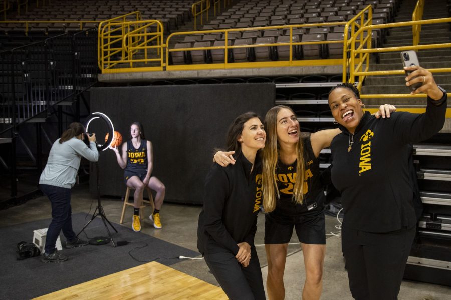 Iowa assistant coach Raina Harmon, Director of Player Development Kathryn Reynolds and Iowa guard Kate Martin takes a selfie with Iowa guard Caitlin Clark in the background during Iowa women’s basketball media day at Carver-Hawkeye Arena in Iowa City on Thursday, Oct. 28, 2021. 