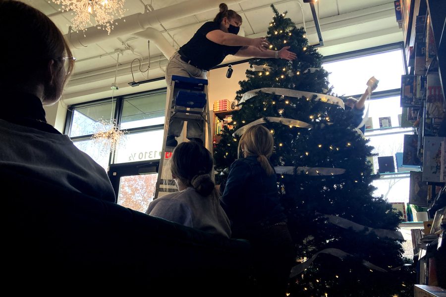 Patrons look on as Assistant Manager Zoe Murphy reaches for ribbon while decorating a tree for the holidays at Sidekick Coffee & Books on Tuesday, Nov. 9, 2021. Murphy is a graduate student studying library science at the University of Iowa, and she has worked at the coffee shop and bookstore since August. She laughed as staff members threw ribbon around the tree. “We’re just vibing,” she said.