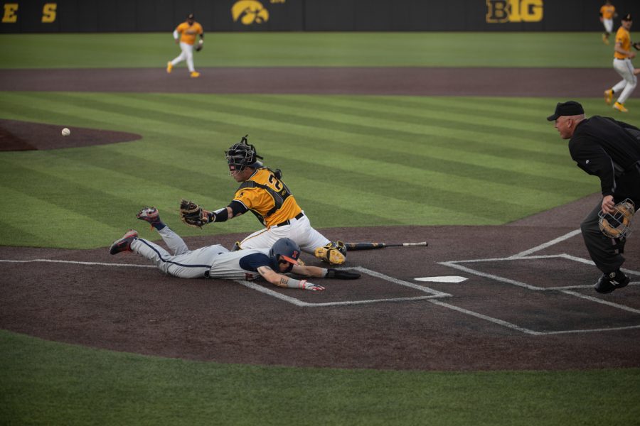 An Illinois base runner scores off a wild throw from right field during a baseball game between Iowa and Illinois at Duane Banks Field on Sunday, April 10, 2022.  The Fighting Illini defeated the Hawkeyes, 9-5.