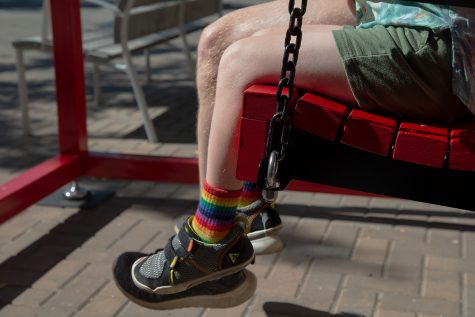 An Iowa City community member wears socks with pride colors on the swing installation on the pedestrian mall in Iowa City during the Pride Festival on Saturday, June 18, 2022.