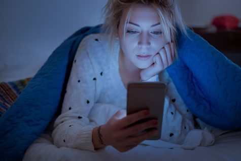 Disappointed sad woman holding mobile phone while laying on bed at night.