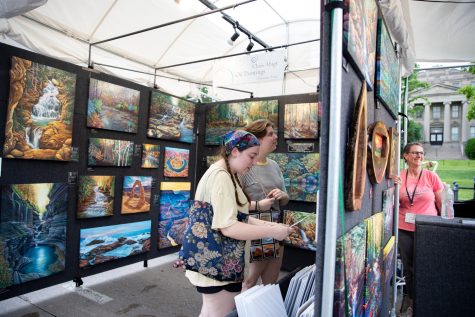Iowa City residents look at Chris Abigt’s oil paintings in downtown Iowa City during day one of the 2023 Summer of the Arts Festival on Friday, June 2.