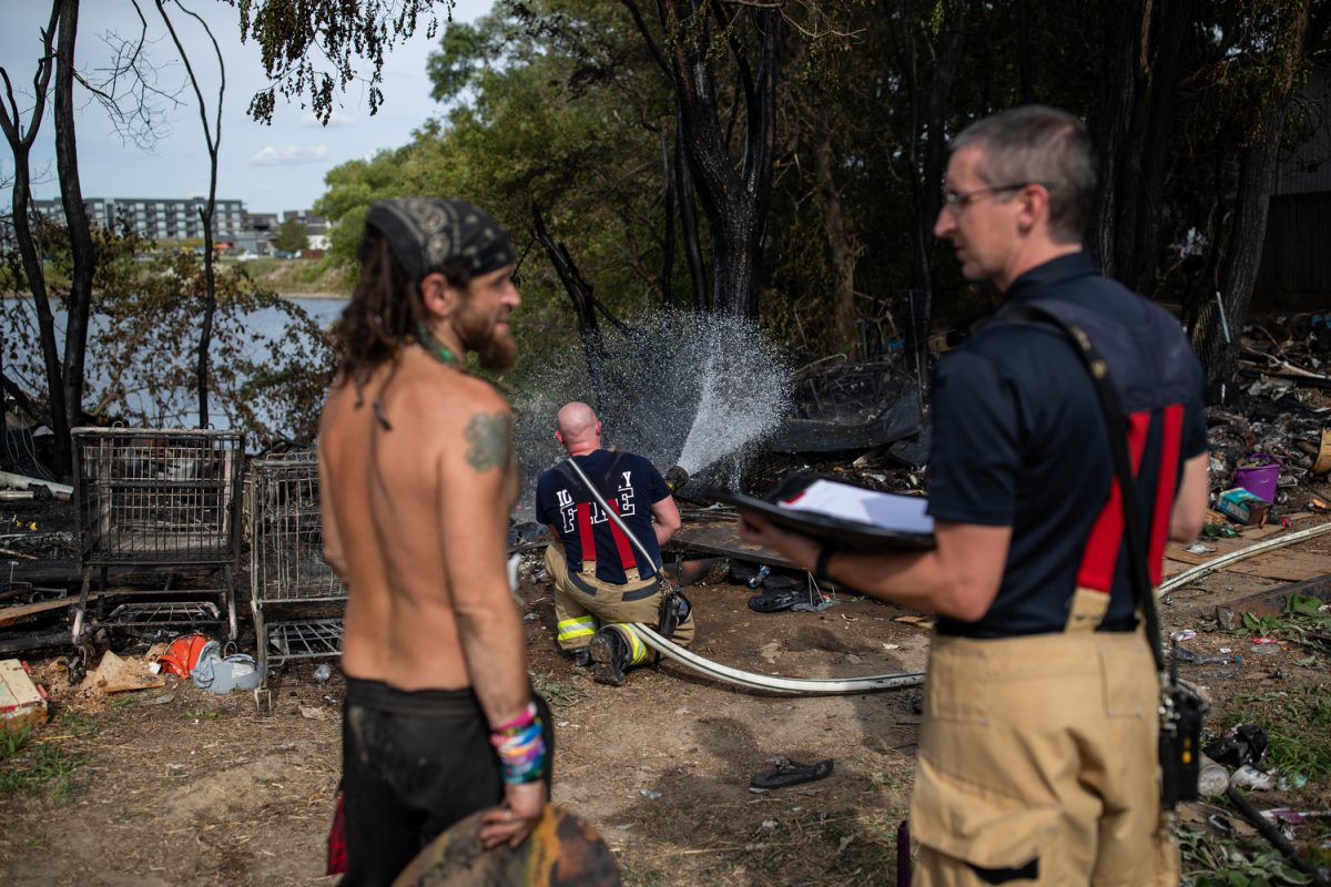Michael talks with an Iowa City Firefighter while another Firefighter continues to dose any remaining embers after an active fire at near a river encampment in Iowa City, on Wednesday, Oct. 4, 2023. 