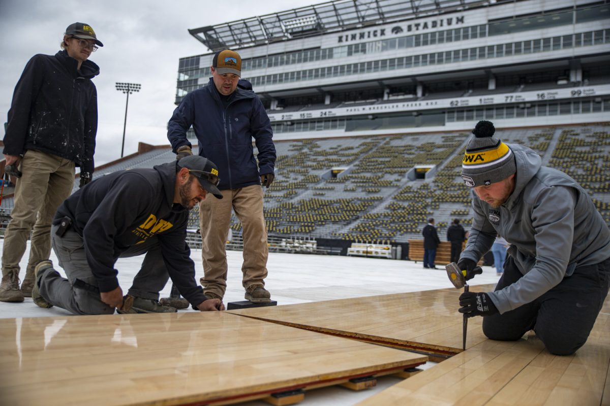 Grounds crew employee Patrick Schmelzle uses a hammer during the assembly of the basketball court for Iowa women’s basketball’s Crossover at Kinnick on Saturday, Oct. 14, 2023.