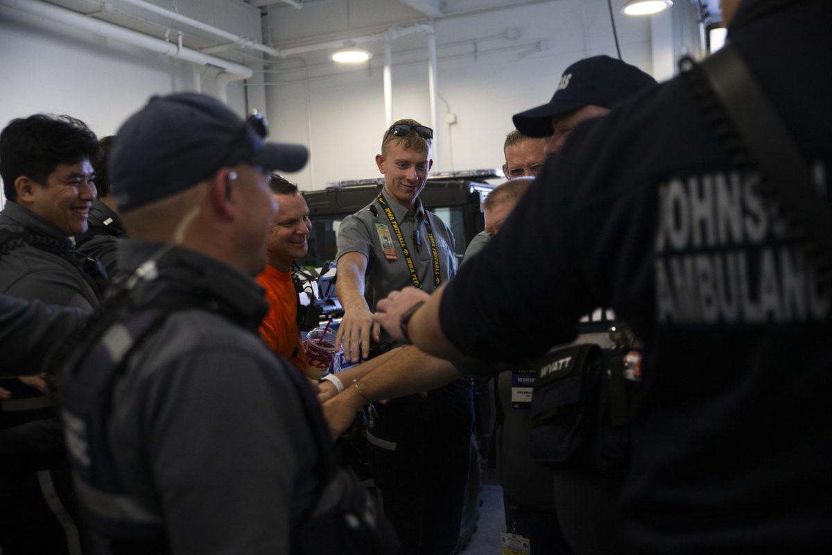 EMS workers unite their hands before leaving for the football game between Iowa and Minnesota at the Johnson County Ambulance Medical Examiner Building on Saturday, Oct. 21, 2023. Each responder working at a football game undergo a four-hour training of protocols, procedures and to familiarize the location in and around Kinnick before the start of every football season. 