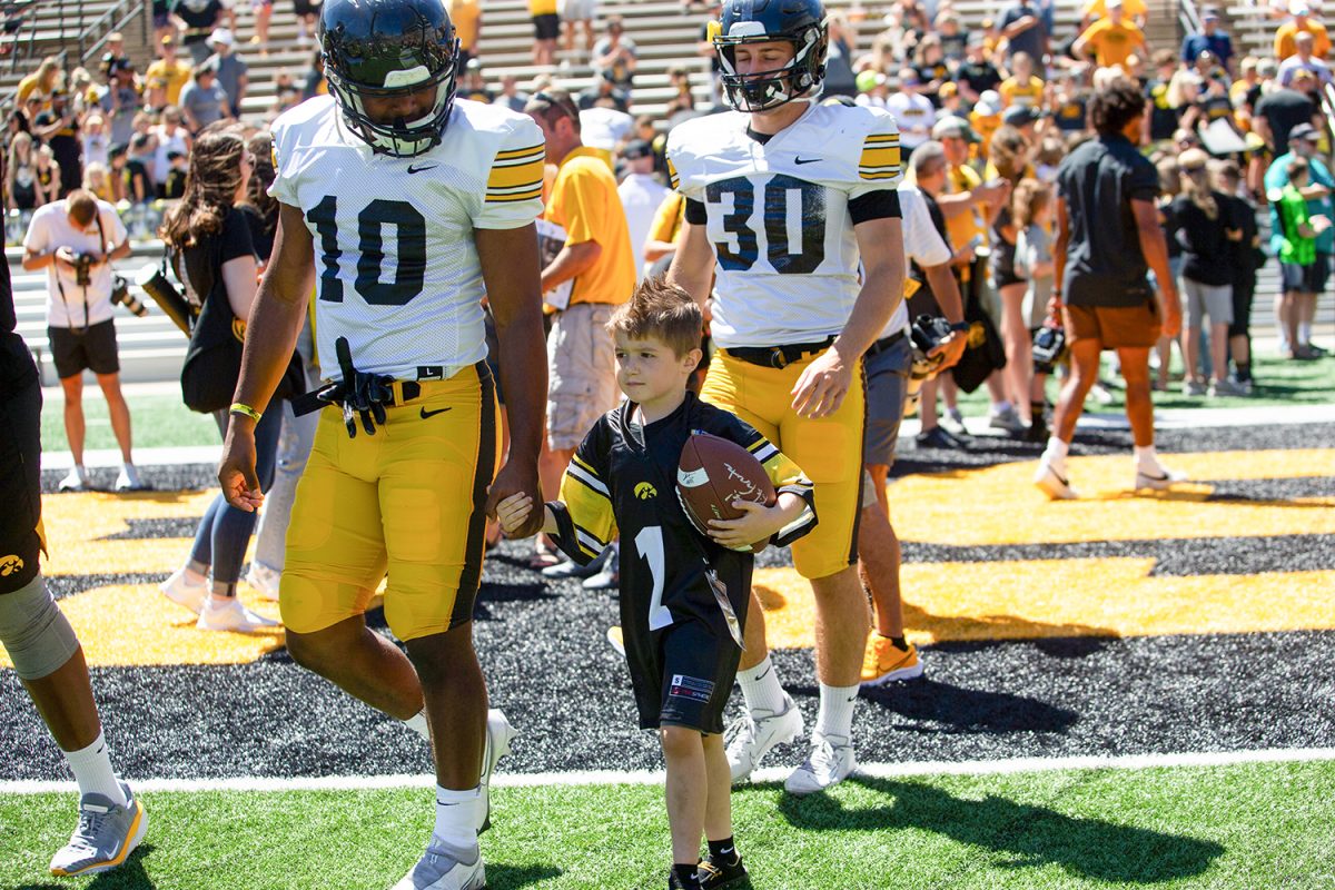Kid captain Lincoln Veach holds linebacker Nick Jackson’s hand during Kids’ Day at Kinnick in Iowa City on Saturday, Aug. 12, 2023. 