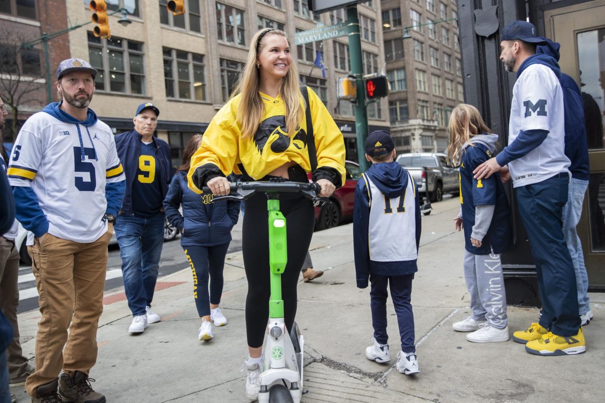 Zoee Moore rides a scooter thorugh a group of Michigan fans before a football game between No.18 Iowa and No. 2 Michigan at Lucas Oil Stadium in Indianapolis on Saturday, Dec. 2, 2023.