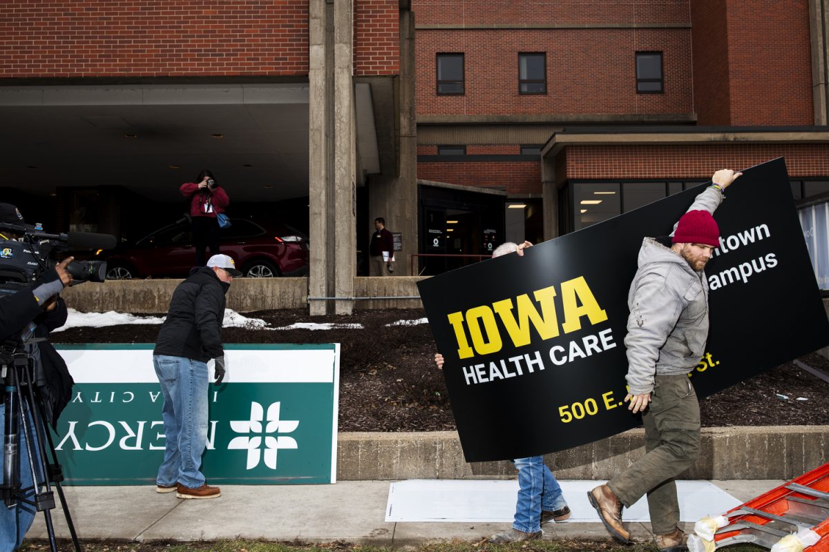 Latitude workers carry a new Iowa Health Care sign during a Mercy signage changing at the University of Iowa Health Care Medical Center Downtown Campus in Iowa City on Wednesday, Jan. 31. 