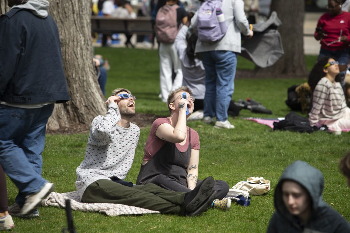Two people share a pair of torn solar viewers during the eclipse watch party on the Pentacrest on Monday, April 8, 2024.