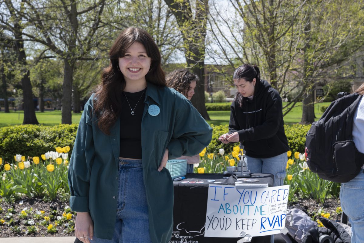 Anna Behrens poses for a portrait while tabling for the Women’s Resource and Action Center (WRAC) on the Pentacrest in Iowa City on Friday, April 19, 2024. Behrens is a Student Violence Prevention Program Assistant for WRAC.