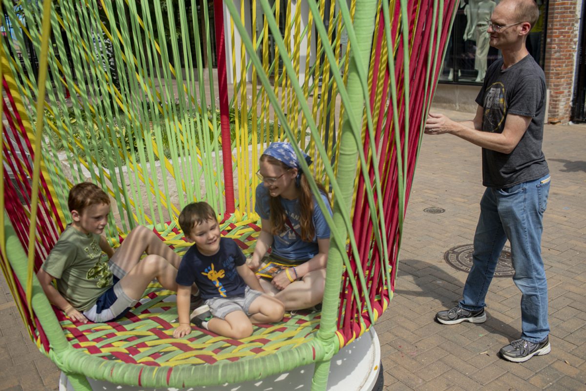 Jack (Left), Calvin, (Center), Gwen (Right) are spun in the Los Trompos art installation by their father, Adam Rabb, in downtown Iowa City on Tuesday, July 16, 2024. 