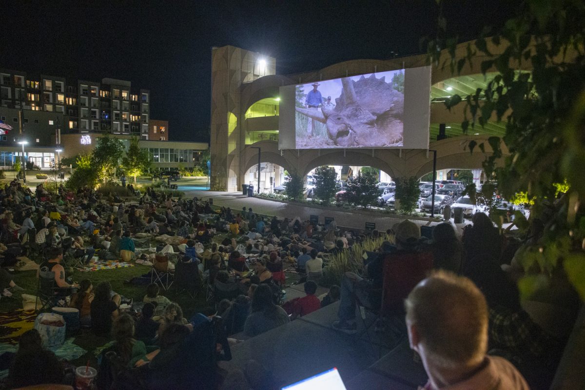 Audience members watch a dinosaur onscreen during a free outdoor showing of Jurassic Park run by FilmScene in the Park in Iowa City on Oct 5. This was their final outdoor movie screening of the summer.