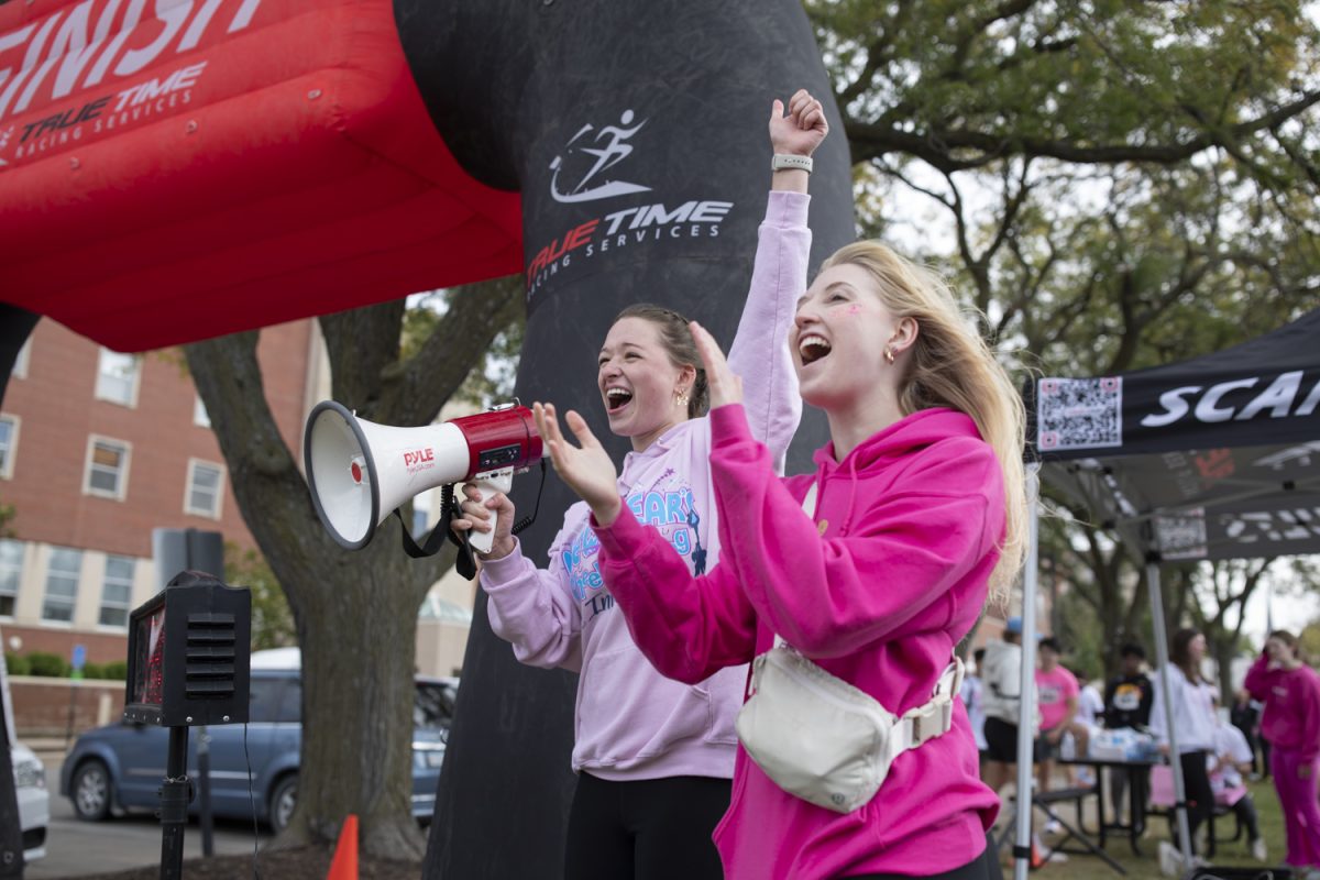 Marissa Majewski and Charlie Brink cheer through a megaphone for runners crossing the finish line during the Zeta Tau Alpha 25th 5K run for breast cancer education and awareness in Iowa City on Sunday, Oct. 13, 2024. The sorority raised almost $20,000 and had over 100 participants.